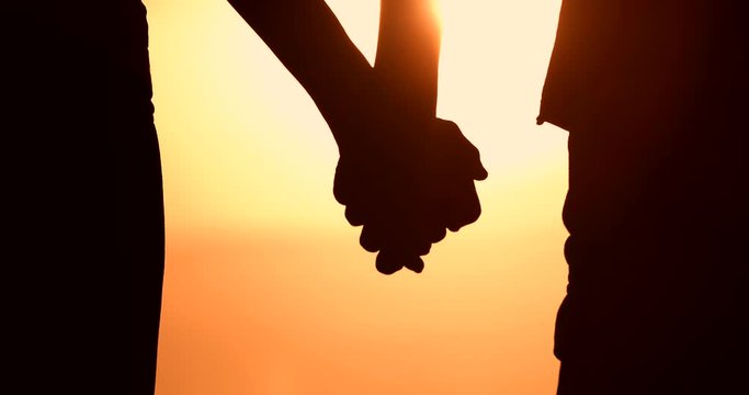 Silhouette of couple holding hands at sunset. Man and woman's hands slowly coming together. People love and relationships. 