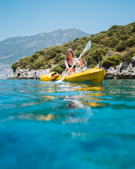 A lone girl paddling a yellow kayak in remote mediterranean waters, exploring the Turkish...