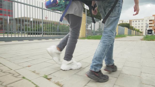 Teenager Girl and Boy walking to school on the sidewalk with a backpack . Close-up of feet. Slow motion video.