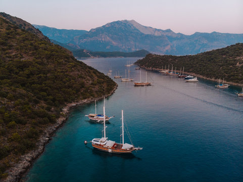 The sun setting over a quiet bay near Fethiye, Turkey. The traditional Turkish gulets line the shore with the mountainous coastal landscape in the background. 