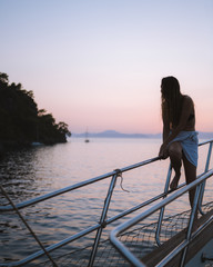 Fototapeta premium Girl relaxing on the side of a yacht watching the sunset in the distance, thinking about life. Shot in antalya coastline, Turkey. 