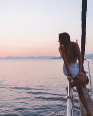 Fototapeta premium Girl relaxing on the side of a yacht watching the sunset in the distance, thinking about life. Shot in antalya coastline, Turkey. 