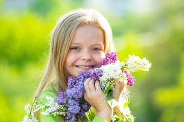 Fototapeta premium Cheerful young little lady in the garden with long fair hair being excited to get a bouquet of lilac on women's day.