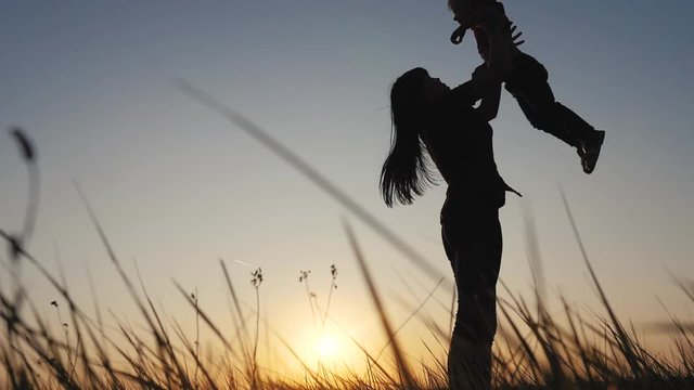 happy family funny a mom holds daughter circling is playing silhouette at sunset slow motion. little girl and woman mom play have fun outdoors sunlight on the field outdoors. teamwork happy family mom