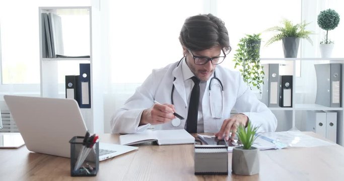 Doctor using laptop while examining xray report and writing notes in diary