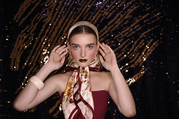 Fashion girl in a textured satin headscarf on head on a gold glitter blurred background....