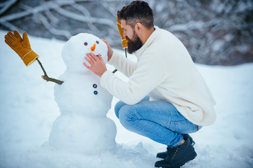 Snowman and funny bearded man in the snow. Man playing with Snowman - isolated on snow background....