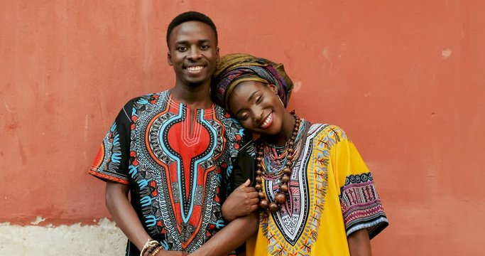 Portrait of the young attractive African woman and man smiling to the camera and hugging in the traditional costumes, woman laying her head on the man's shoulder with love.