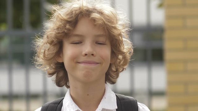 Close up portrait of beautiful , attractive , caucasian curly hair boy with Backpack. School child looking and smiling on the camera.