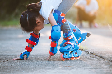 Cute asian child girl riding on roller skates and fall down in the park