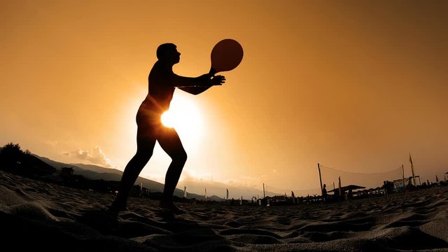 Slow motion of a silhouette of a men playing tenning with a racket on the beach at sunset