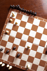 Chess board and pieces on dark brown wooden table.