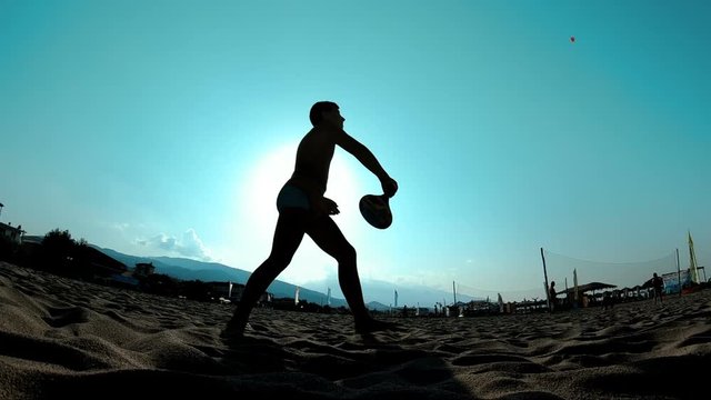 Slow motion of silhouette of men playing ball paddle beach on the sand in the shore of the beach