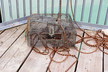 A crab pot lays on a deck with ropes