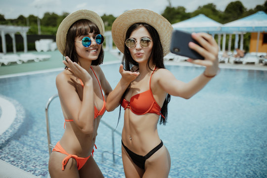 Two pretty woman in swimsuit making selfie photo on smartphone outdoors at pool
