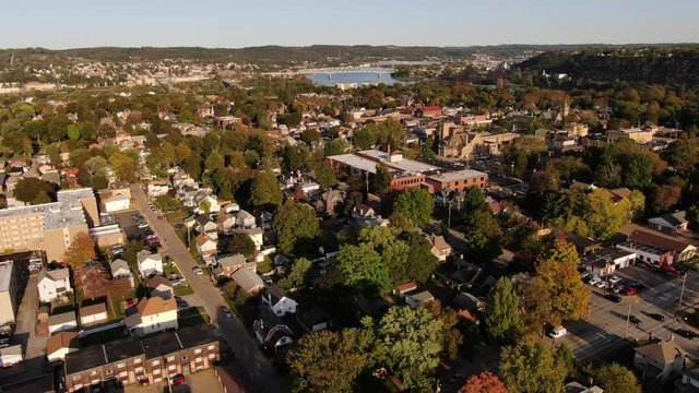 An early evening reverse aerial establishing shot of an upscale residential neighborhood in the Pennsylvania hills. Pittsburgh suburbs. Ohio River in the far distance.  	