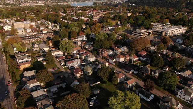 An early evening forward tilting down aerial establishing shot of a residential neighborhood in the Pennsylvania hills. Pittsburgh suburbs. Ohio River in the far distance.  	
