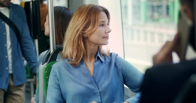 Portrait shot of the Caucasian beautiful young woman in the blue jeans shirt sitting in the tram and looking at the window with a smile.