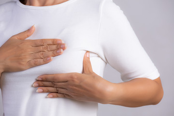 Woman hand checking lumps on her breast for signs of breast cancer on gray background. Healthcare concept.