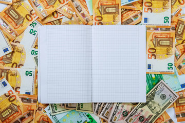 A white notebook with blank pages lay on a set of banknotes of 100 euros, 50 euros and 100 dollars.