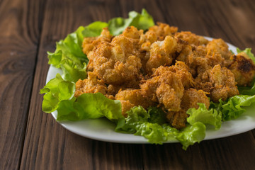 Baked cauliflower on lettuce leaves on a white plate. The view from the top.
