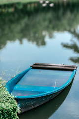 Vertical shot of small blue boat parking on the lake, with forest refelction on the water. Nature vacation concept