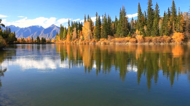 Tranquil beautiful autumn landscape with a reflection of yellowed trees and a mountain range in a wide river on a sunny day. Siberia, Baikal region, Eastern Sayan Mountains,  Buryatia, Tunka valley