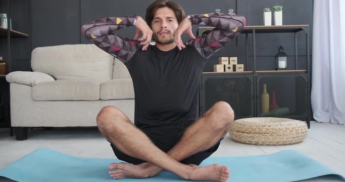 Man in sportswear doing stretching exercise on mat at home
