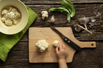 Cooking Cauliflower. Top view, wooden table. The child helps to cook