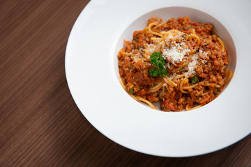 Spaghetti in tomato sauce, served on a plate, parsley in a white dish, on a brown wooden floor,  Italian food