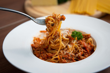 Use a a fork to scoop spaghetti in tomato sauce, served on a plate, parsley in a white dish, on a brown wooden floor Italian food,