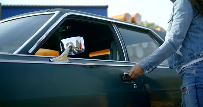 brunette woman is opening door and sitting inside old car in sunny windy day