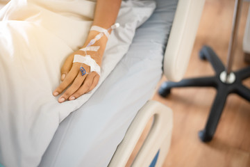 Obraz premium The sick person's hand is wearing a blue dress, lying on the bed in the hospital.