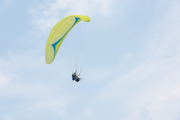 A yellow paraglider flies freely in the blue sky