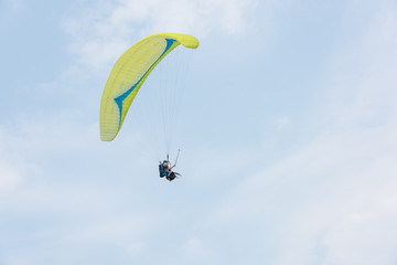 A yellow paraglider flies freely in the blue sky