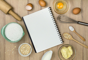 tools and ingredients  for baking cake (flour, butter, eggs, milk, Oatmeal) and  blank notebook on wooden background. Top view.