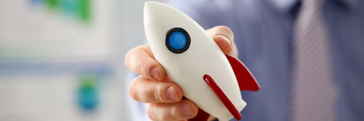 Businessman in suit hold white rocket in hand office background