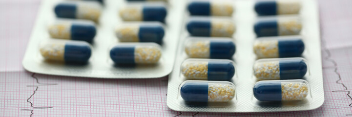 The capsule pill in a blister pack lies on paper printout of medical electrocardiogram concept.
