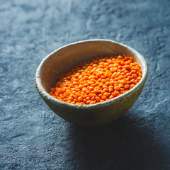 Red lentils in a bowl close up on dark stone background