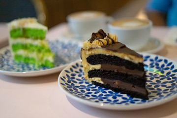 A slice of chocolate cake on the plate with on the background is Gula Melaka cake in green colour. Coffee cake tea time concept.