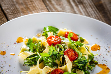 Pasta with tomatoes and arugula on wooden table