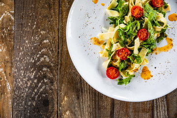 Pasta with tomatoes and arugula on wooden table