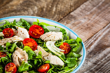Salad with chicken meat and arugula on wooden table