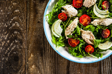 Salad with chicken meat and arugula on wooden table