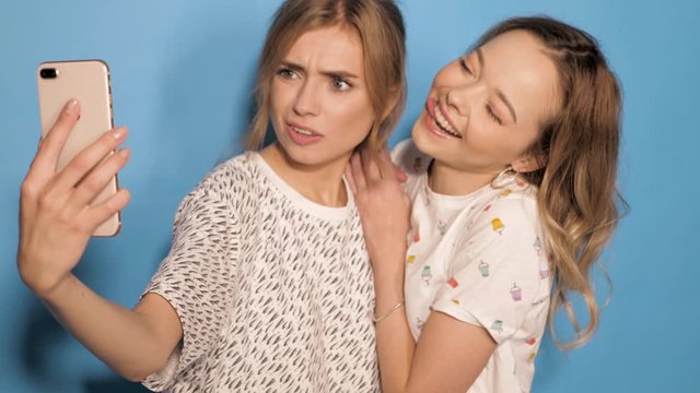 Two beautiful smiling girls.Women in summer hipster clothes taking selfie self portrait photos on smartphone. Models making funny faces and having fun in studio.They show tongue and make duck face