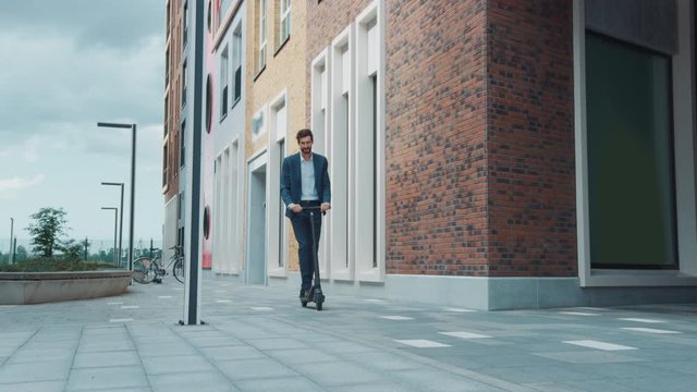Young Businessman in a Suit Riding to Work on an Electric Scooter. Modern Entrepreneur Uses Contemporary Ecological Transport to Go on an Office Meeting. Slow Motion Video.