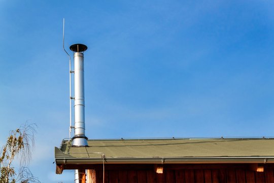 New metal chimney pipe on wooden house. Stainless steel chimney on house. Ecological wood heating. Environment. Lightning conductor on chimney.
