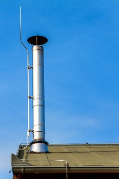New metal chimney pipe on wooden house. Stainless steel chimney on house. Ecological wood heating. Environment. Lightning conductor on chimney.