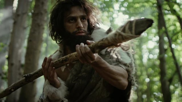 Portrait of Primeval Caveman Wearing Animal Skin and Fur Hunting with a Stone Tipped Spear in the Prehistoric Forest. Prehistoric Neanderthal Hunter Ready to Throw Spear in the Jungle