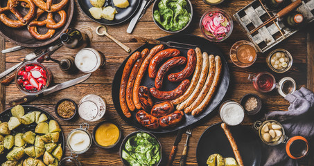 Flat-lay of Octoberfest dinner table concept with grilled veal and pork sausages, pretzel pastry,...